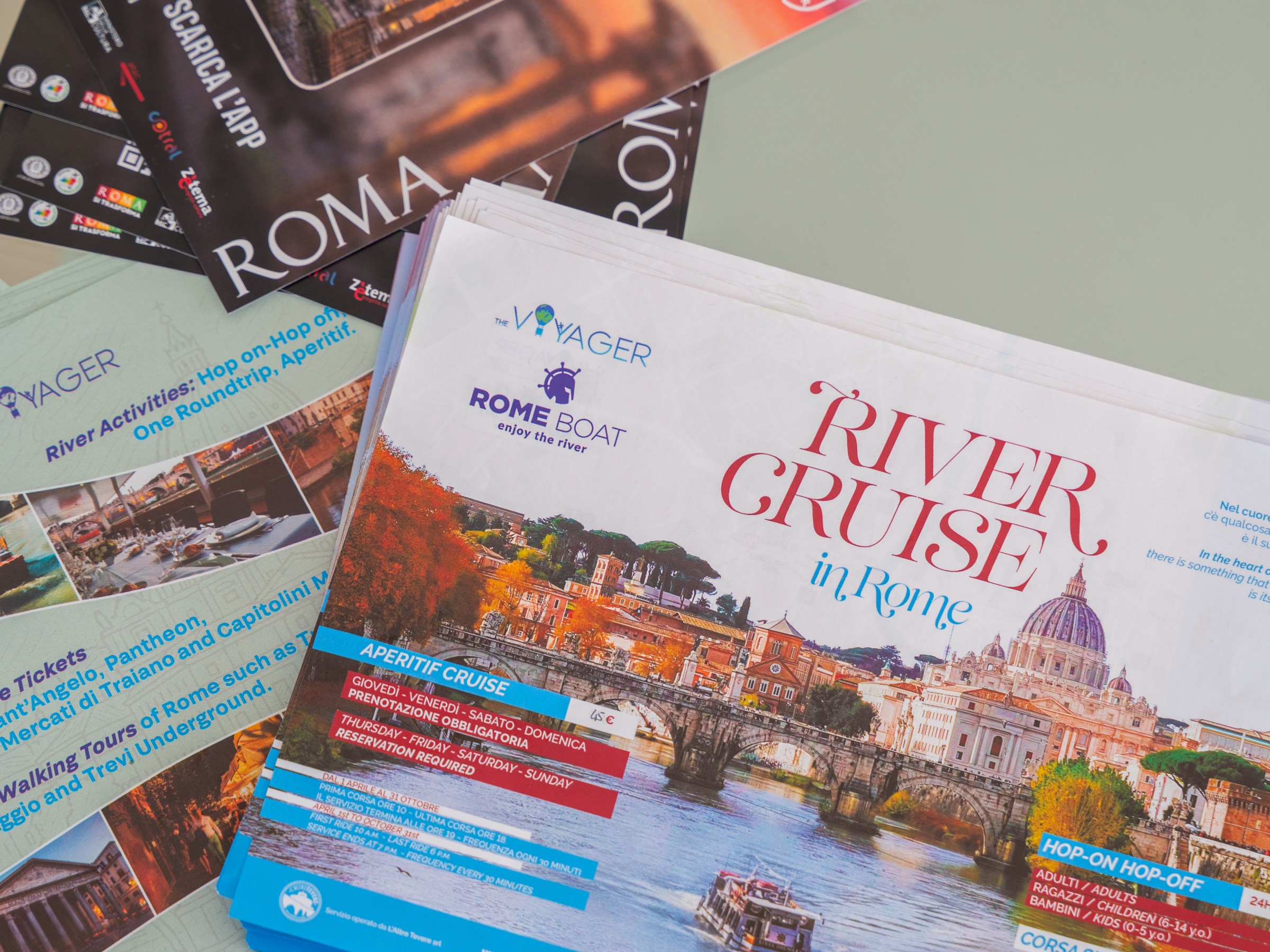 Stack of brochures for 'River Cruise in Rome' and Roma Pass on a table.
