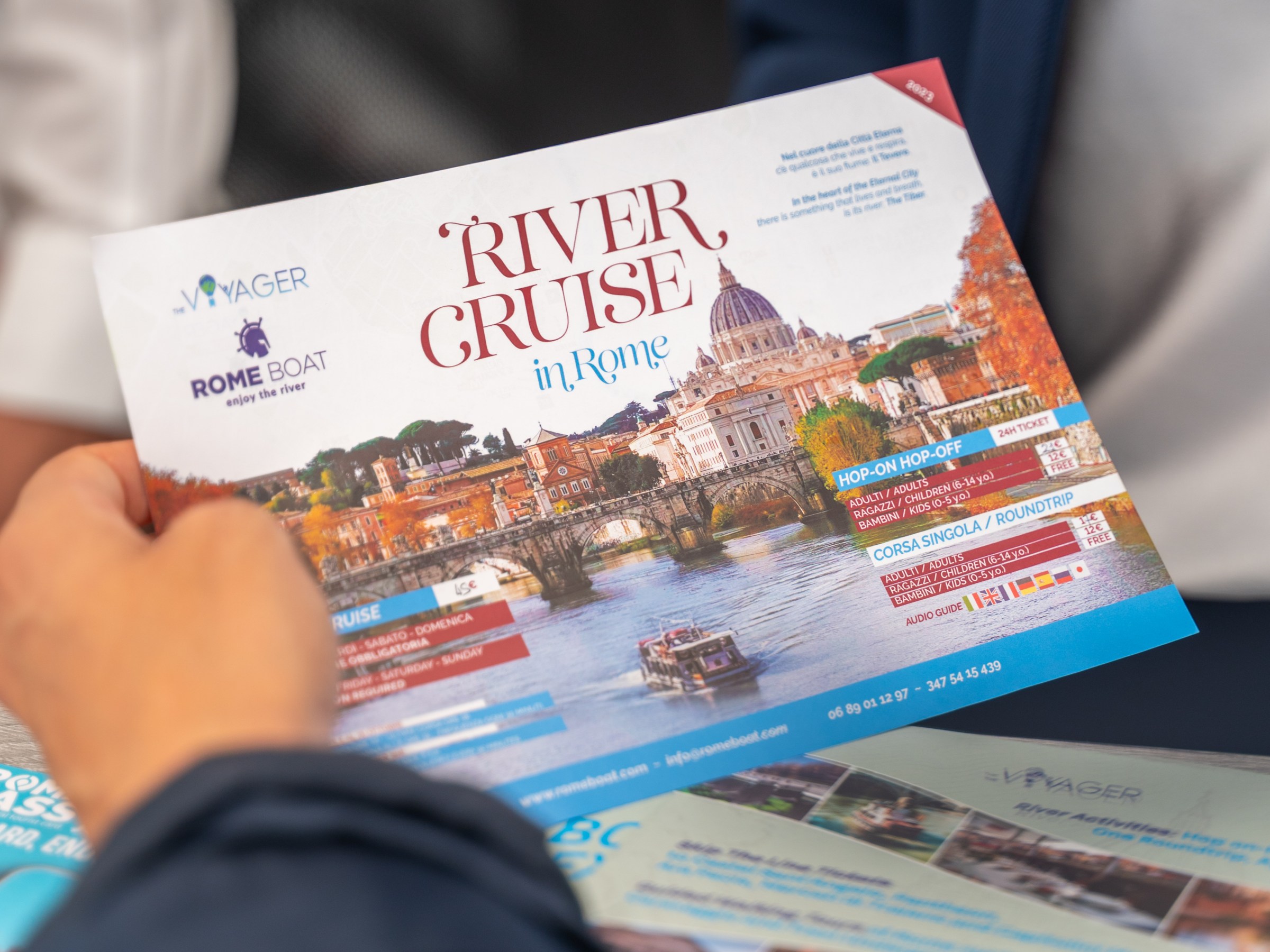 Person holding a brochure titled 'River Cruise in Rome' with scenic river and city image.
