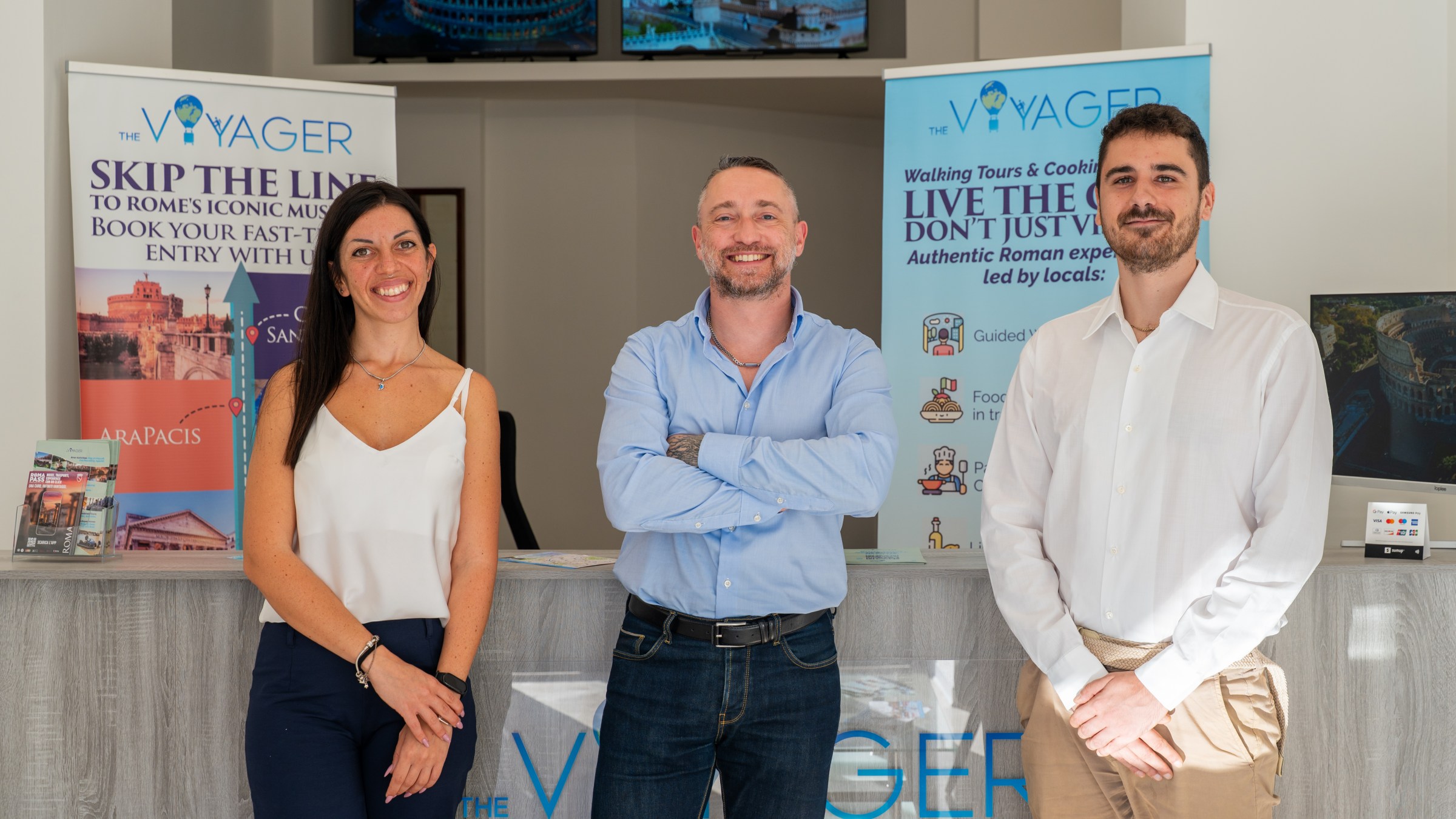 Three people smiling at a travel agency counter with promotional posters.