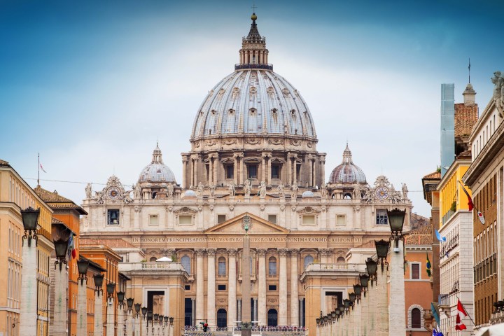 St. Peter's Basilica facade under a clear blue sky, with surrounding buildings.